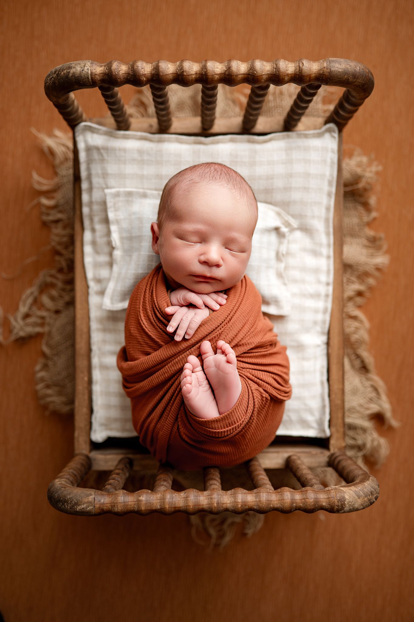 Peaceful newborn sleeping swaddled in soft blue fabric on a velvet pillow in vintage wooden crib.