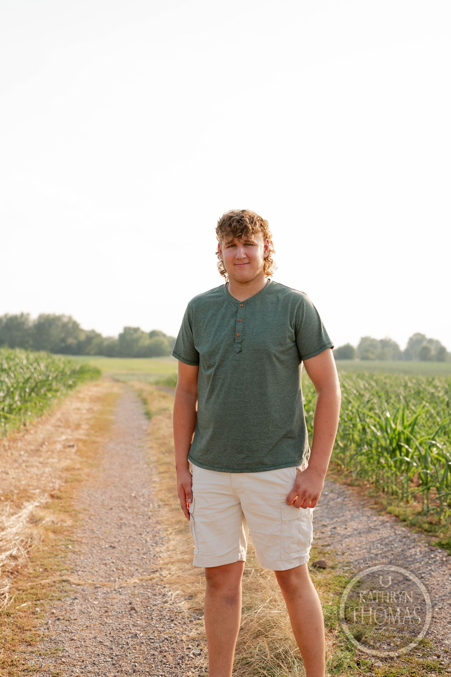 Person in green henley and khaki shorts stands on a rural dirt path.
