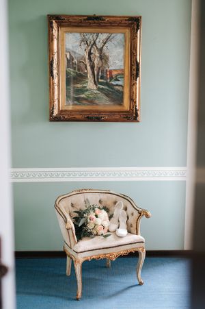 Vintage gold-framed settee with bridal bouquet beneath an ornate painting in an elegant room.