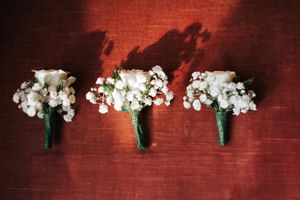 Three delicate white baby's breath and rose boutonnieres arranged in a row on a red surface.