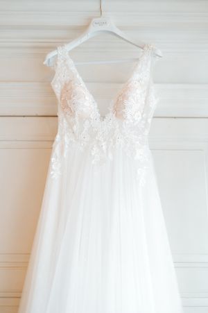 Stunning white A-line wedding dress with deep V-neck and intricate floral lace bodice on hanger.