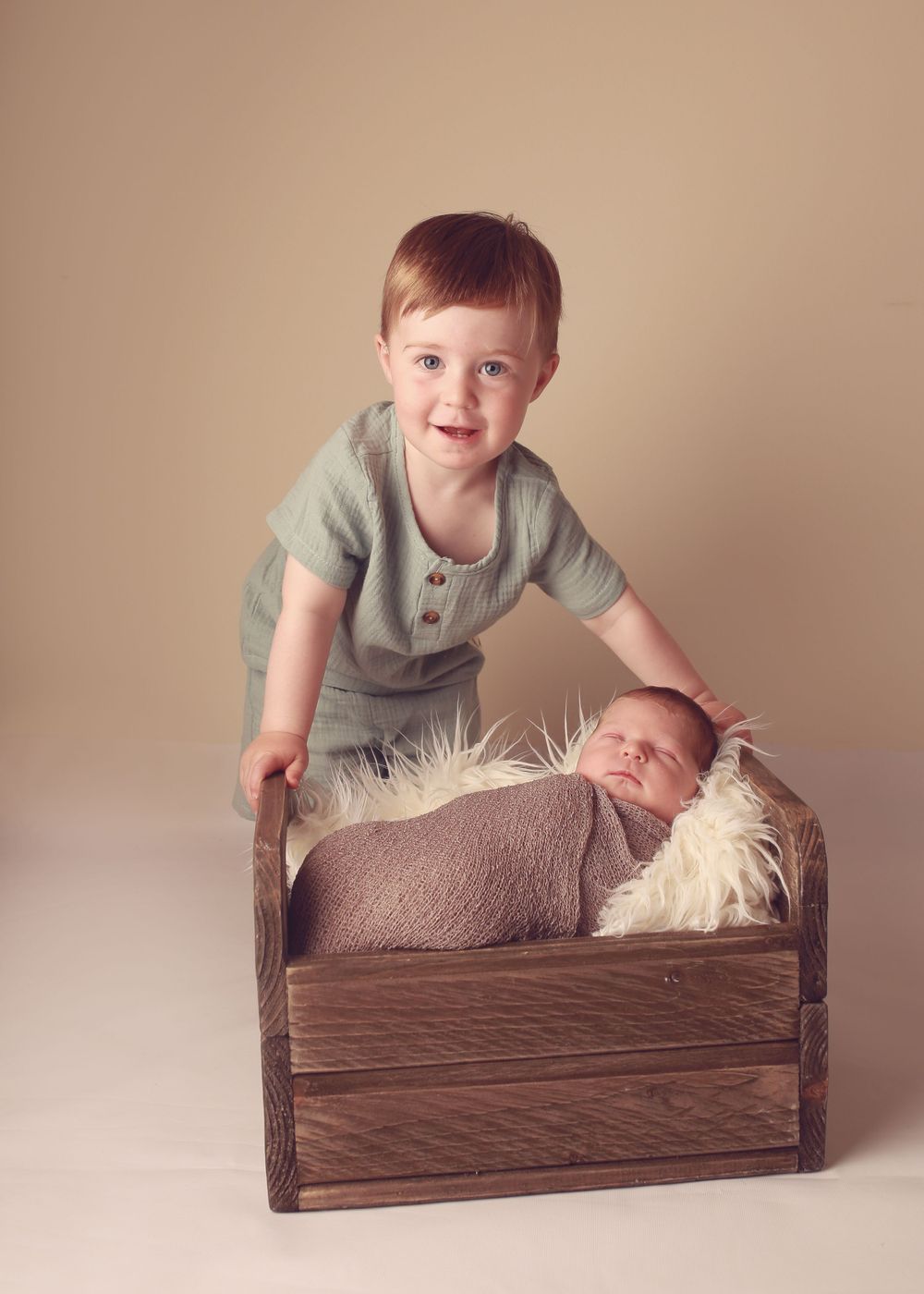 An older brother gently holding his newborn sibling, capturing a sweet and tender moment of brotherly love during a newborn photo session