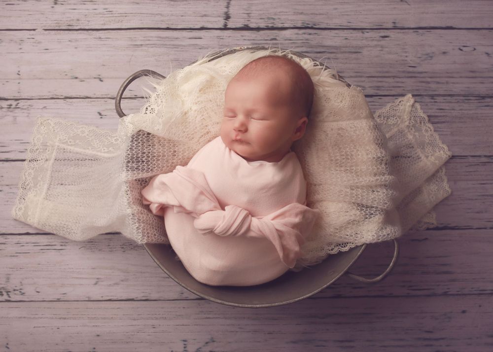A peaceful newborn baby girl wrapped in soft fabrics, captured in a serene and intimate setting, showcasing the delicate beauty in photo