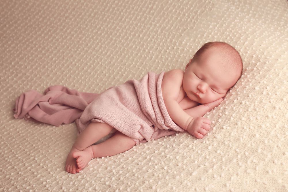 A peaceful newborn baby girl wrapped in soft fabrics, captured in a serene and intimate setting, showcasing the delicate beauty in photo