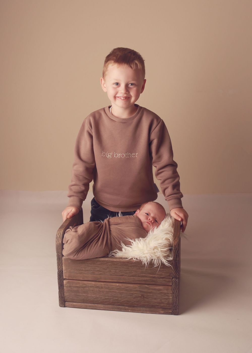 An older brother gently holding his newborn sibling, capturing a sweet and tender moment of brotherly love during a newborn photo session