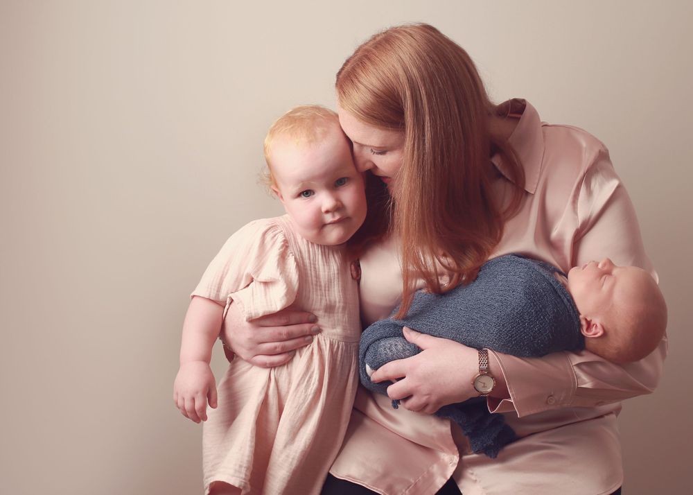 A heartwarming moment of a mother with her toddler and newborn, capturing the beautiful bond and love during a family photo session