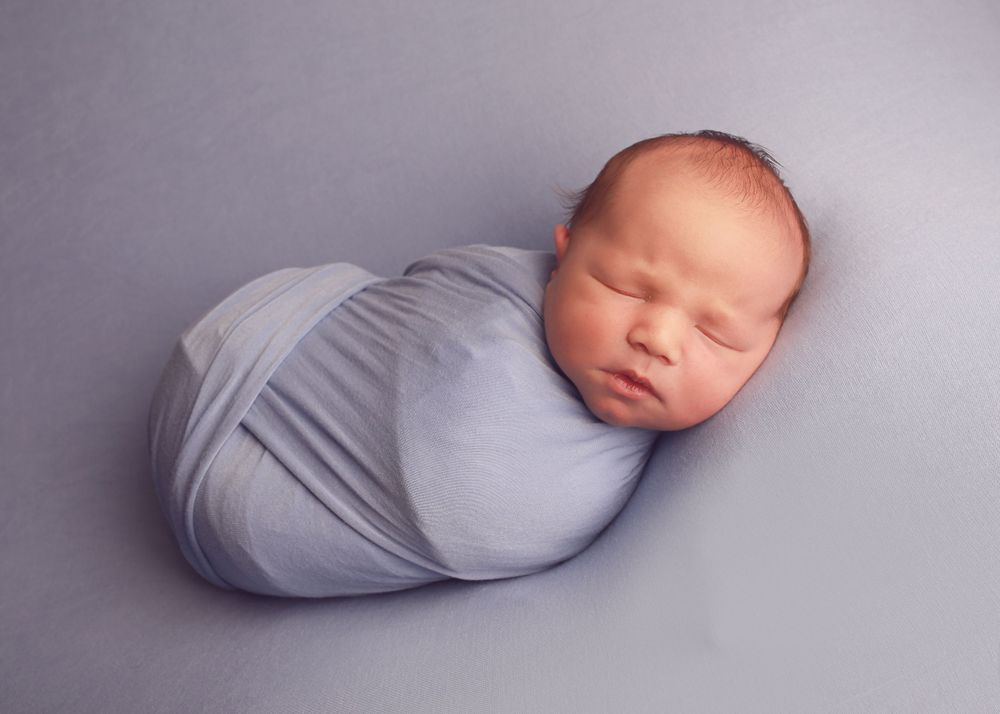 A peaceful newborn baby wrapped in soft fabrics, captured in a serene and intimate setting, showcasing the delicate beauty of early life