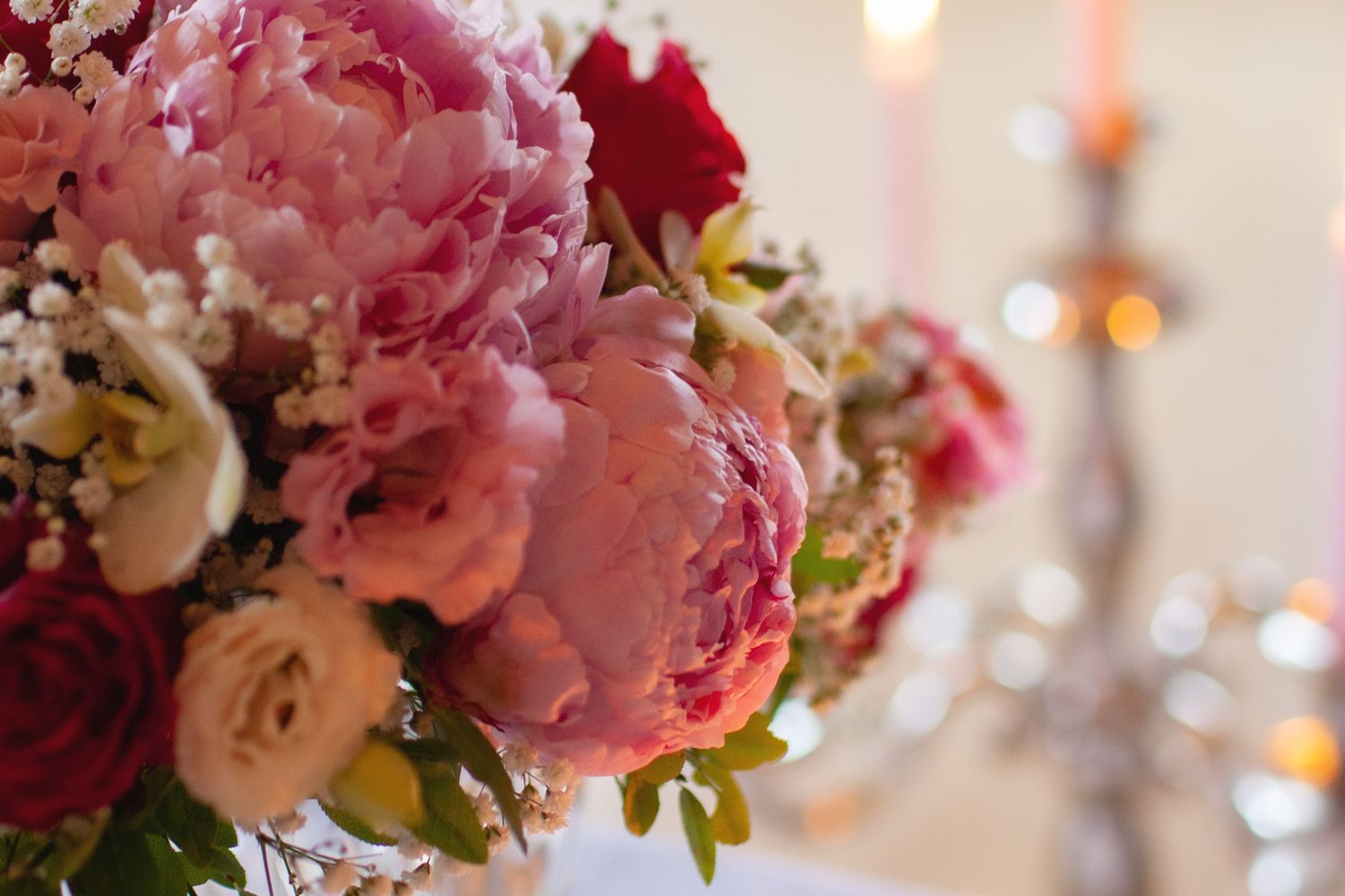 Beautiful arrangement of pink peonies and roses in soft focus with candlelight.