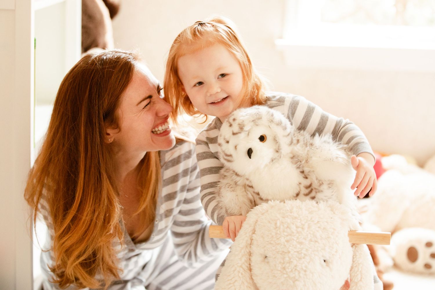 A parent and child share a tender moment at home while holding a large plush stuffed animal.