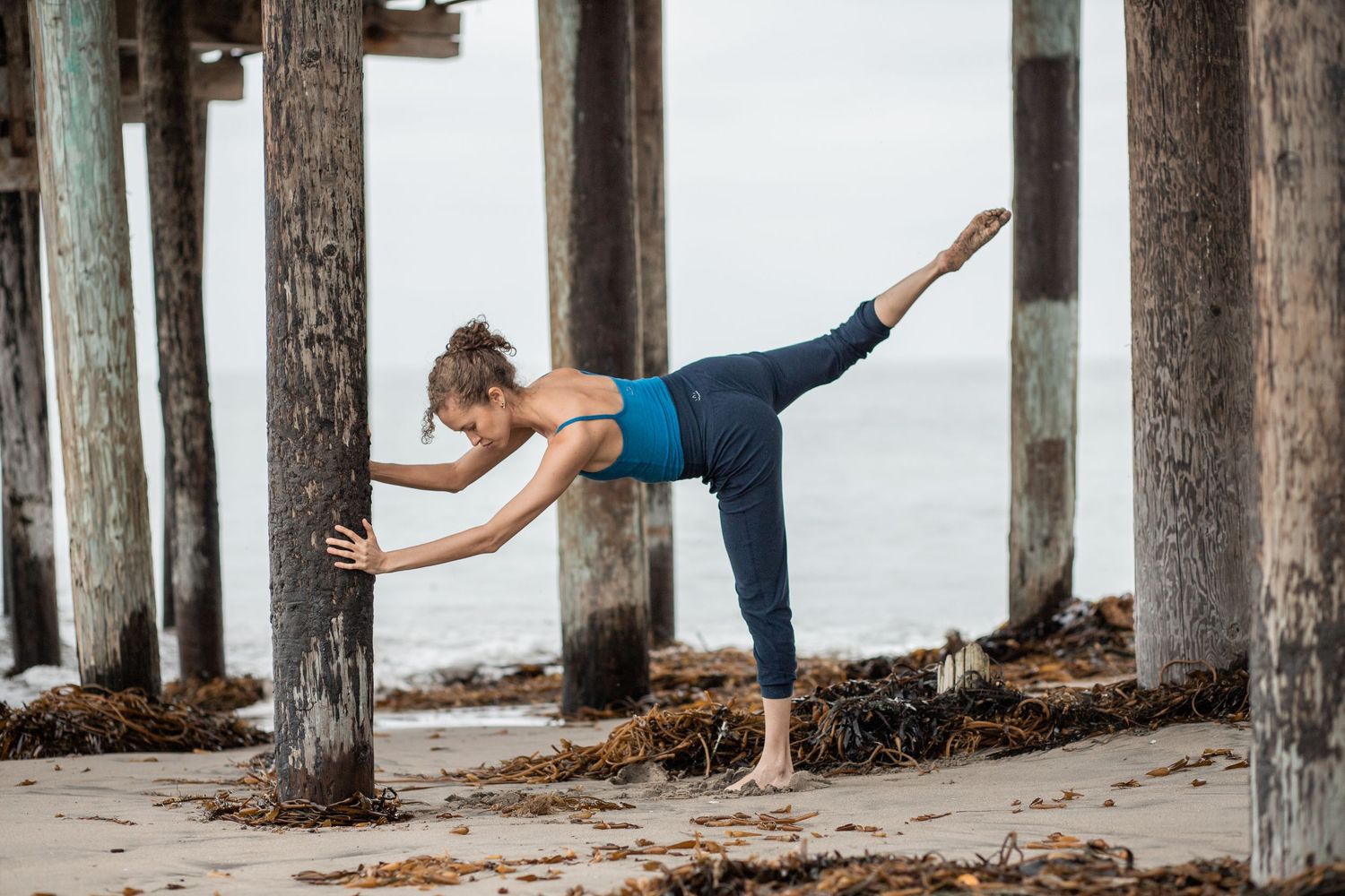 Woman doing stretch against wooden ocean pillar