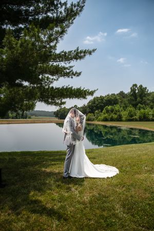 A romantic lakeside wedding photo with pine trees and blue skies in the background.