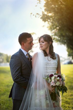 A romantic outdoor wedding portrait of a couple in golden sunlight with the bride holding a bouquet of roses.
