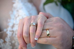 Close-up of wedding rings and clasped hands showing intricate engagement ring and wedding bands.