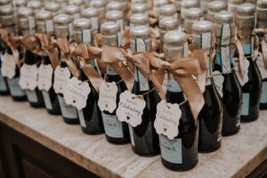 Rows of small wedding favor bottles with tags and ribbons arranged on a wooden table.