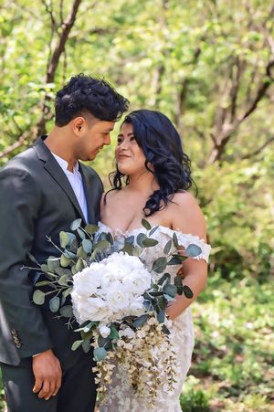 Wedding couple embracing outdoors with bride holding white floral and eucalyptus bouquet.