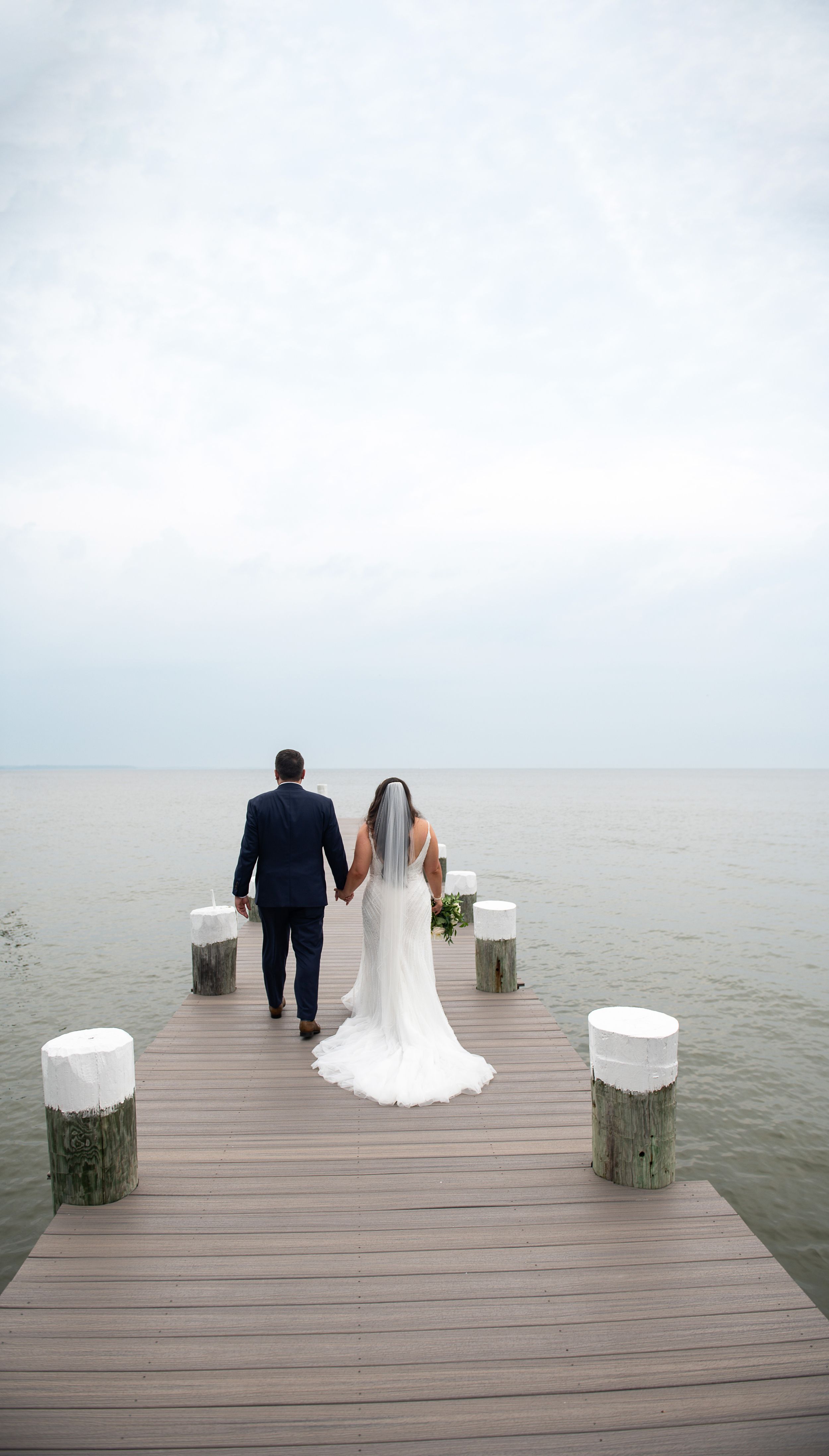A serene wedding photo of newlyweds walking on a dock over calm waters.