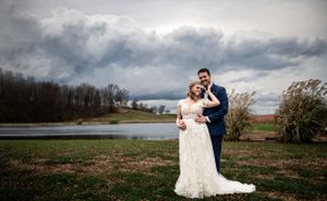 Wedding couple posing near a lake with dramatic storm clouds in the background.