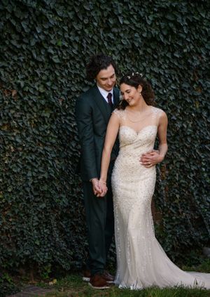 Elegant couple in formal attire posing against ivy wall backdrop during wedding photoshoot.