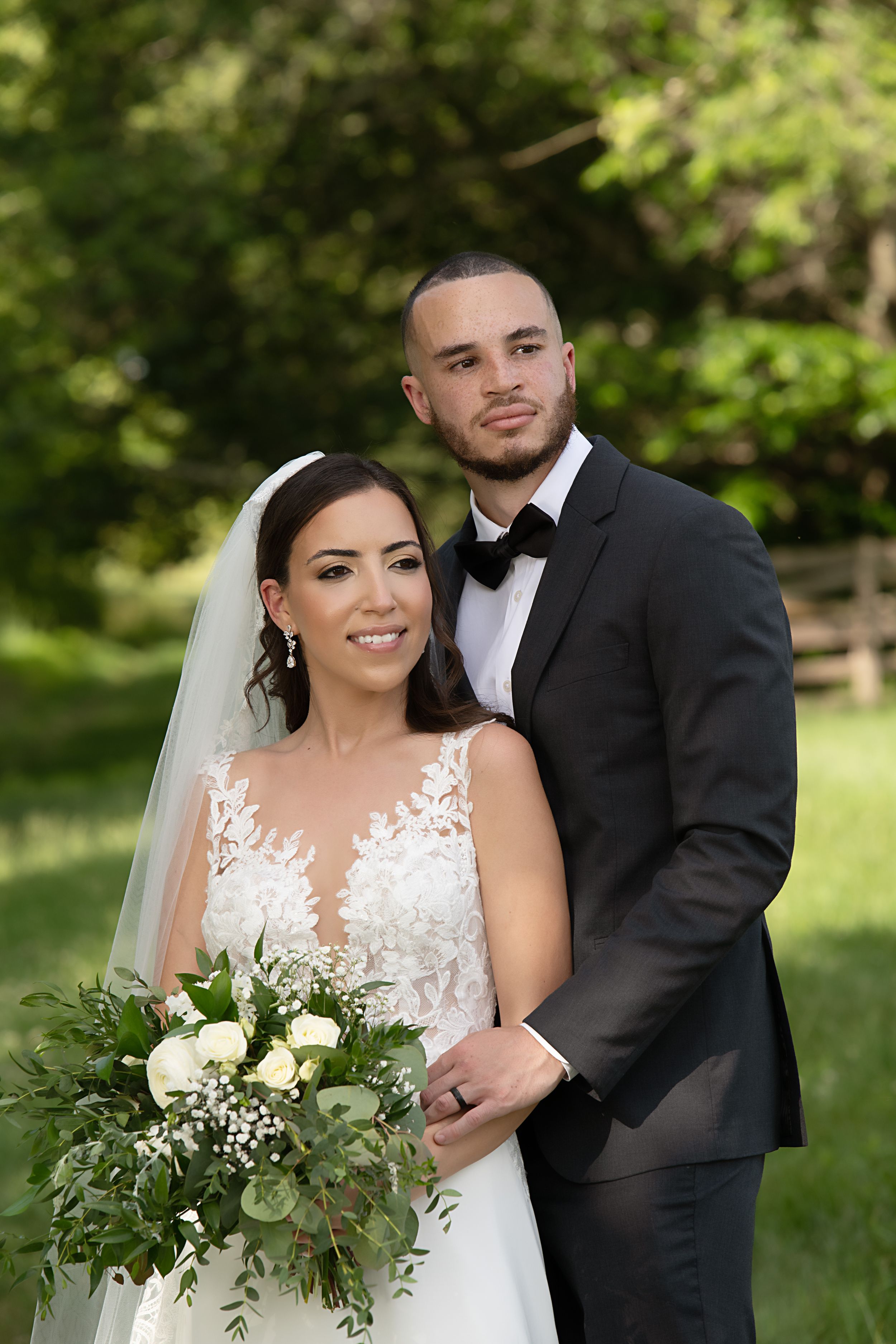 An elegant outdoor wedding portrait with the couple holding a lush white and green bouquet.