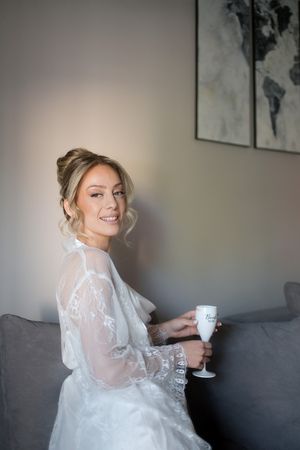 Elegant bridal preparation scene with white lace robe and champagne glass on grey couch.