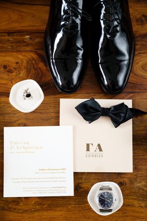 Elegant black leather dress shoes and formal wedding invitation details arranged on a rustic wooden surface.