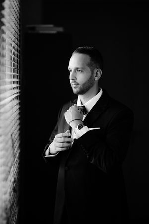 Dramatic black and white portrait series showing a person in formal attire against dark background with window light.