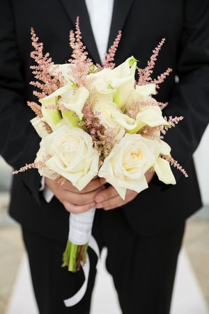 Close-up of an elegant wedding bouquet featuring cream roses and pink astilbe against a black tuxedo.