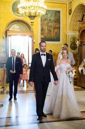 A wedding party walks through an ornate golden ballroom with crystal chandeliers and classical artwork on the walls.