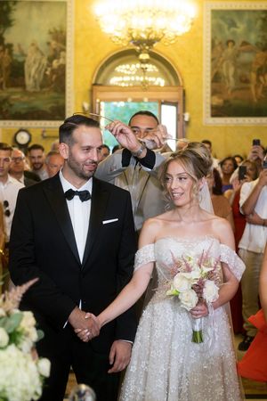 Elegant wedding ceremony in a grand yellow-walled room with ornate chandeliers and classical artwork.