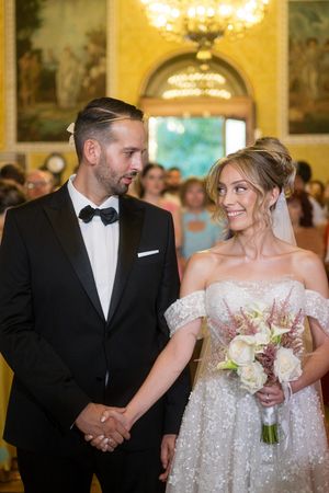 Wedding couple walking down aisle in luxurious ballroom with golden walls and crystal chandeliers.
