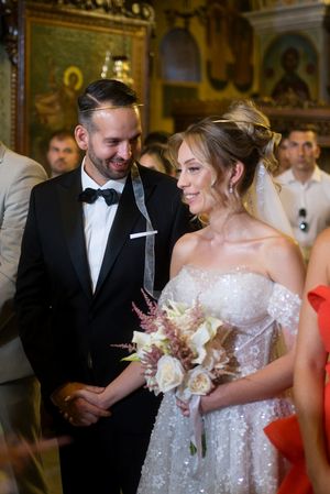 A couple shares a joyful moment during their wedding ceremony in an ornate church with gilded icons in the background.