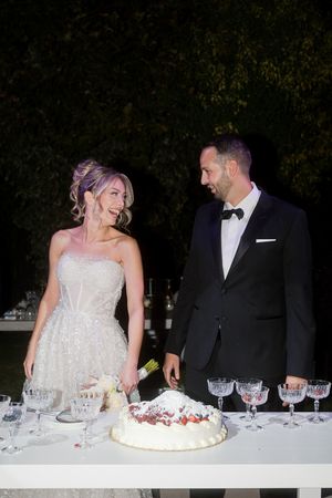A couple in formal wedding attire cuts their white wedding cake together at an elegant evening reception.