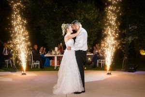 A couple dances under sparkling fireworks at an outdoor evening wedding reception.