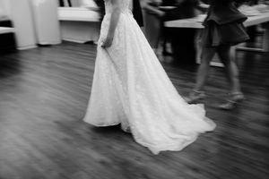 A couple shares their first dance at a wedding reception on a dark wooden dance floor.