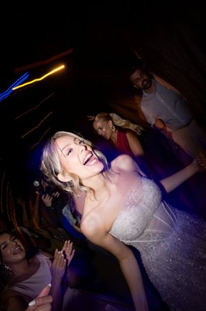 A person in a white dress dances energetically on a dark dance floor with colorful lighting.