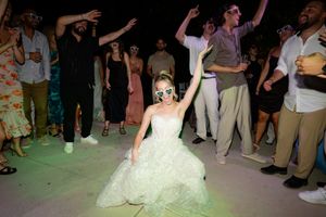 A bride in a white wedding dress dances with guests on a crowded dance floor during a wedding reception celebration.