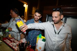 Bartenders mix drinks at a nightclub bar using yellow and green mixers and cocktail ingredients.