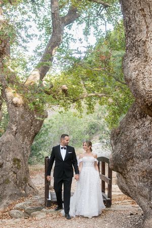 A bride and groom walk hand in hand along a tree-lined path during their outdoor wedding ceremony.