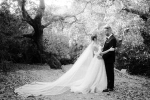 A couple in wedding attire embraces under blooming trees in a romantic black and white garden setting.
