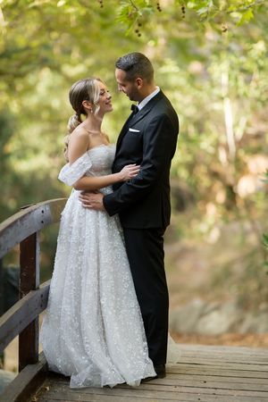 A romantic wedding couple shares intimate moments on a wooden bridge surrounded by autumn foliage.