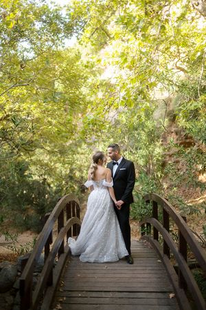 A couple shares romantic moments on a rustic wooden bridge surrounded by lush green foliage.
