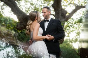 Newlyweds embrace under the canopy of a large tree during an outdoor photo session.