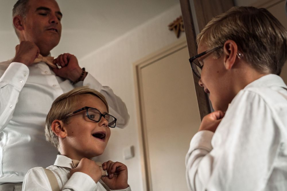 Three people in white shirts and glasses adjust their bow ties while getting ready.