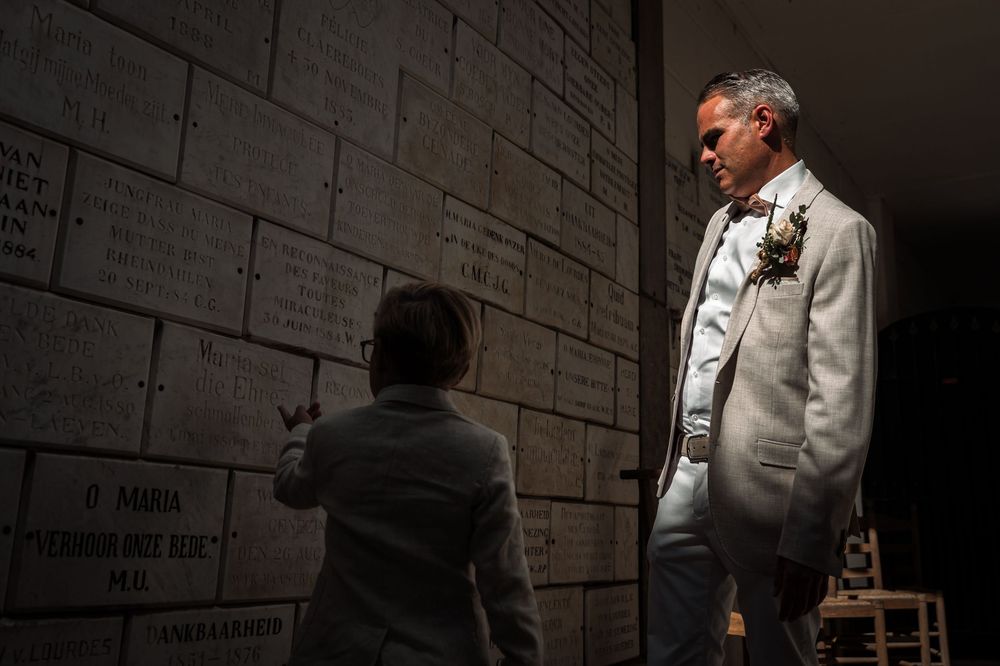 A person in a white shirt stands against a dark concrete wall in dramatic lighting.