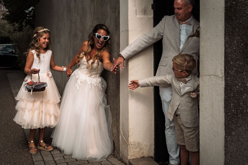 A joyful wedding moment captured with people laughing together on stone steps, with elegant white dresses and formal attire.