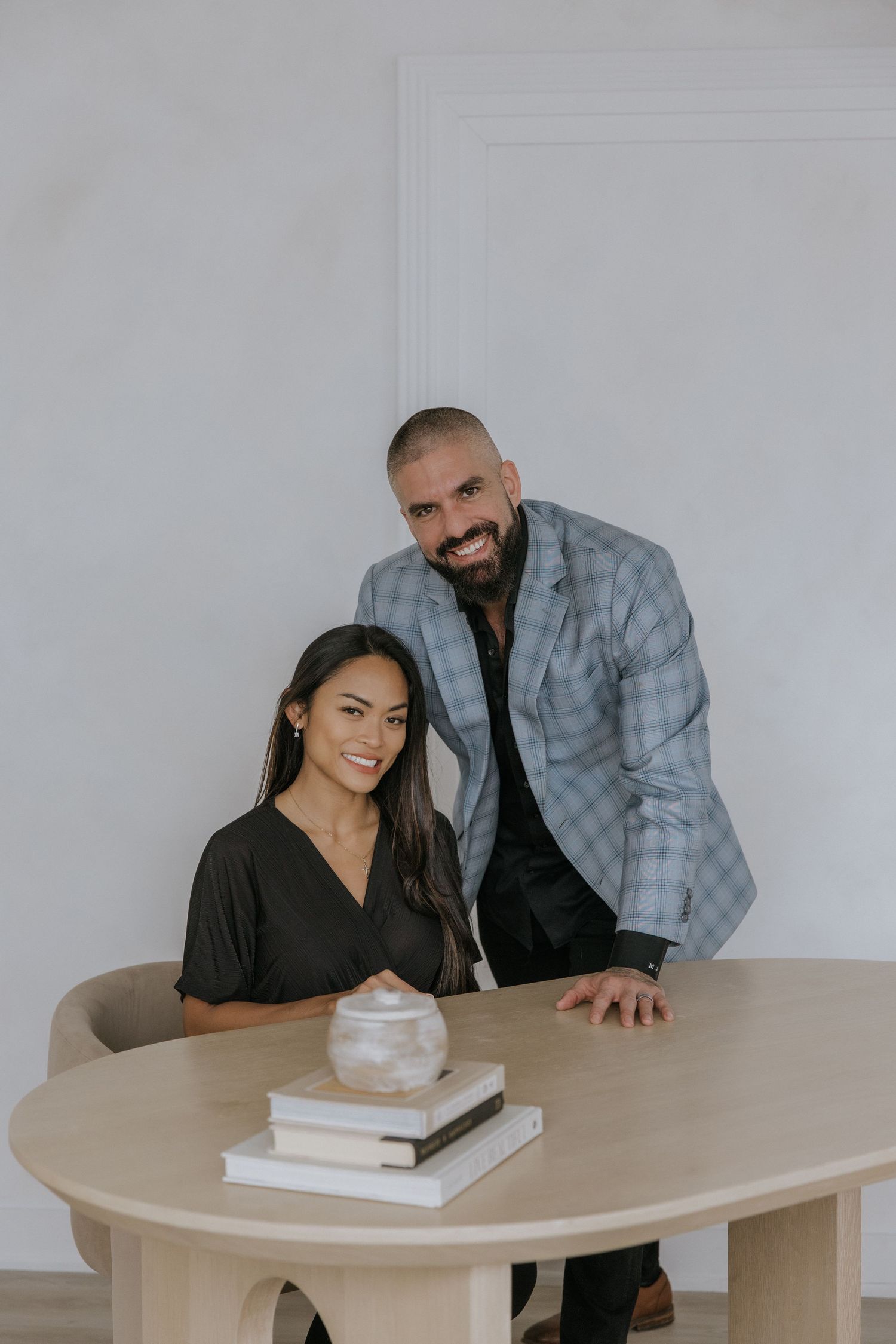 Two people sit at a round wooden table in a minimalist white room, leaning in to review documents together.