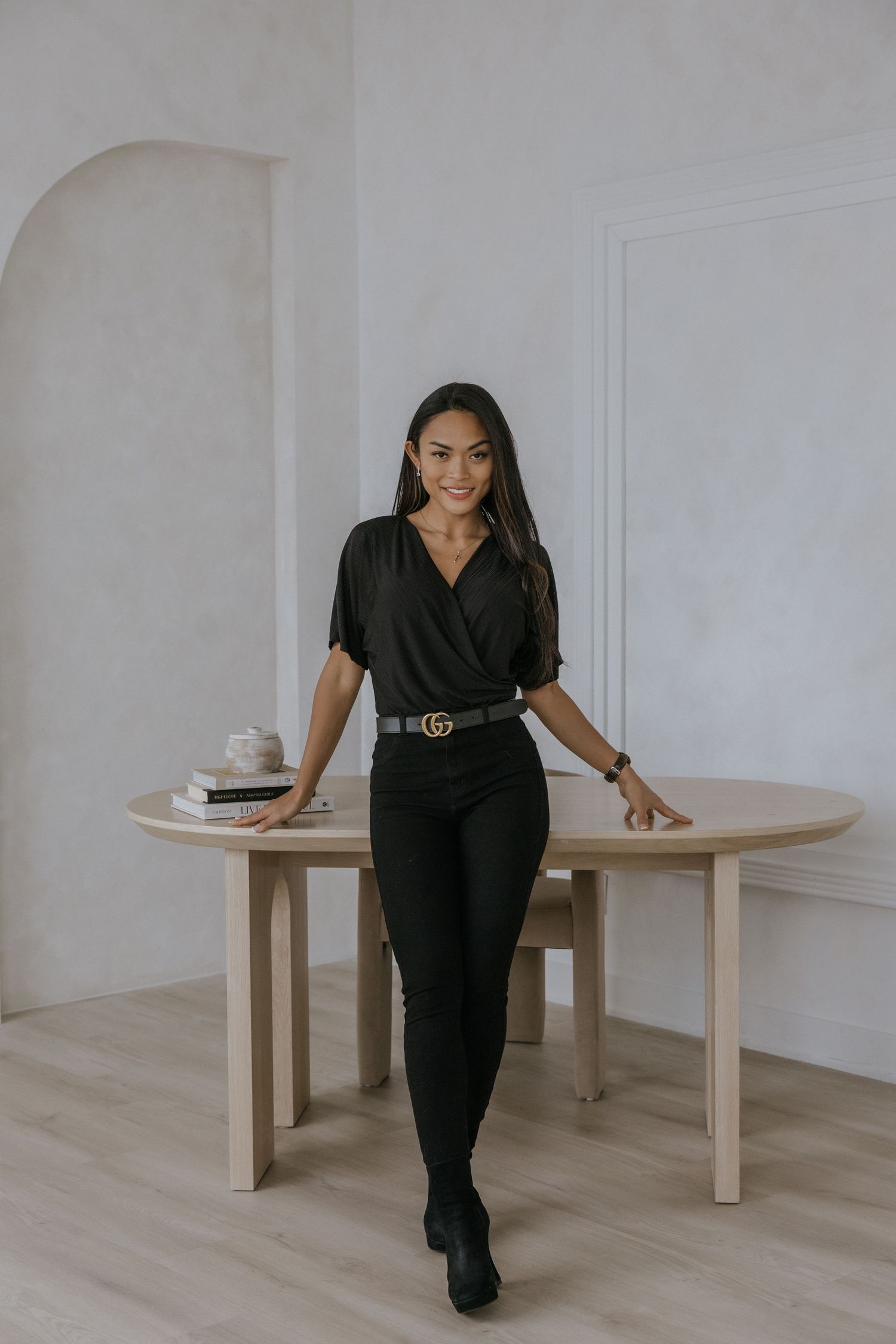 Creative lifestyle photos of someone in black outfit interacting with round wooden tables in minimal setting.