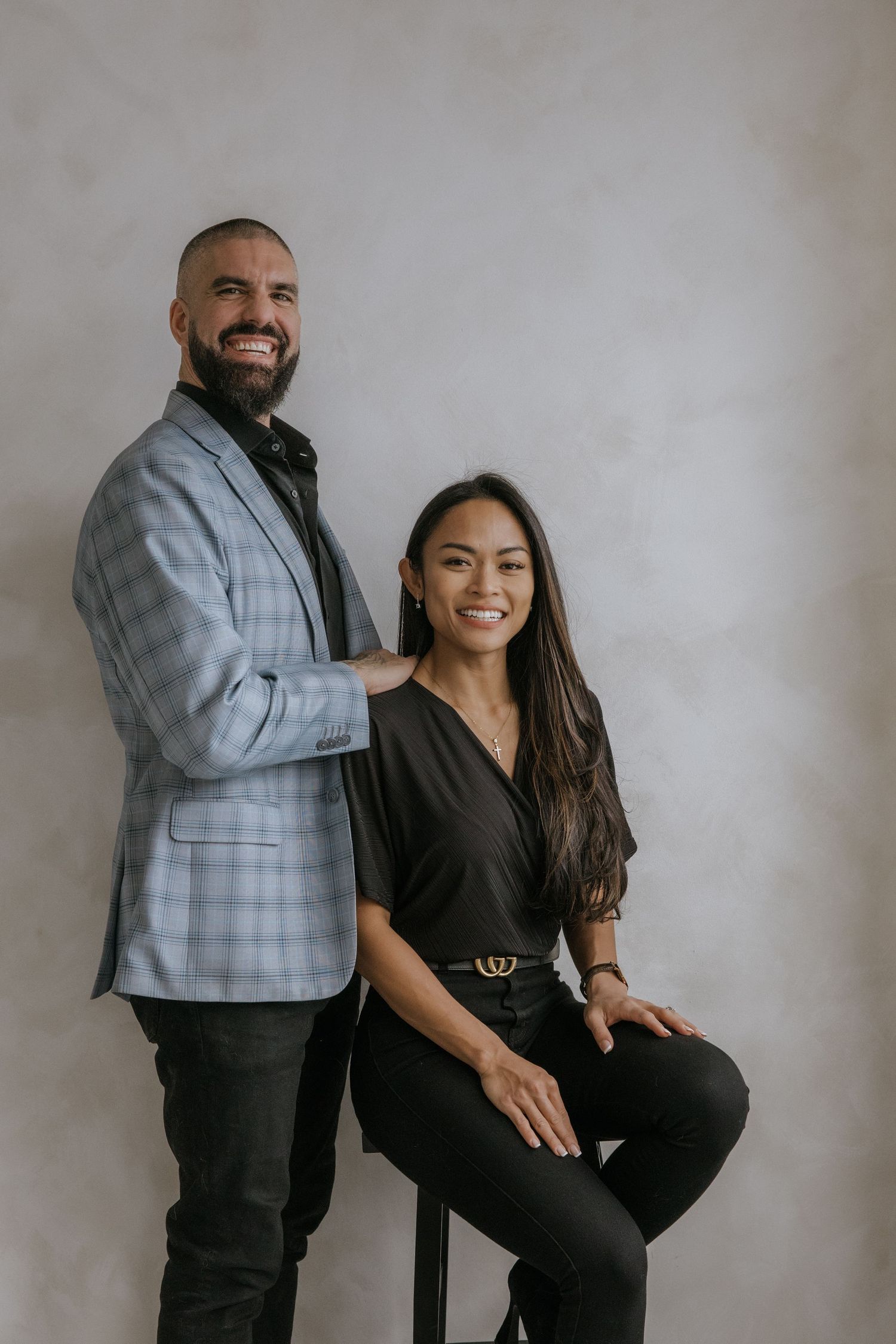 A couple poses together against a gray backdrop in a series of candid lifestyle portraits showing playful interactions.