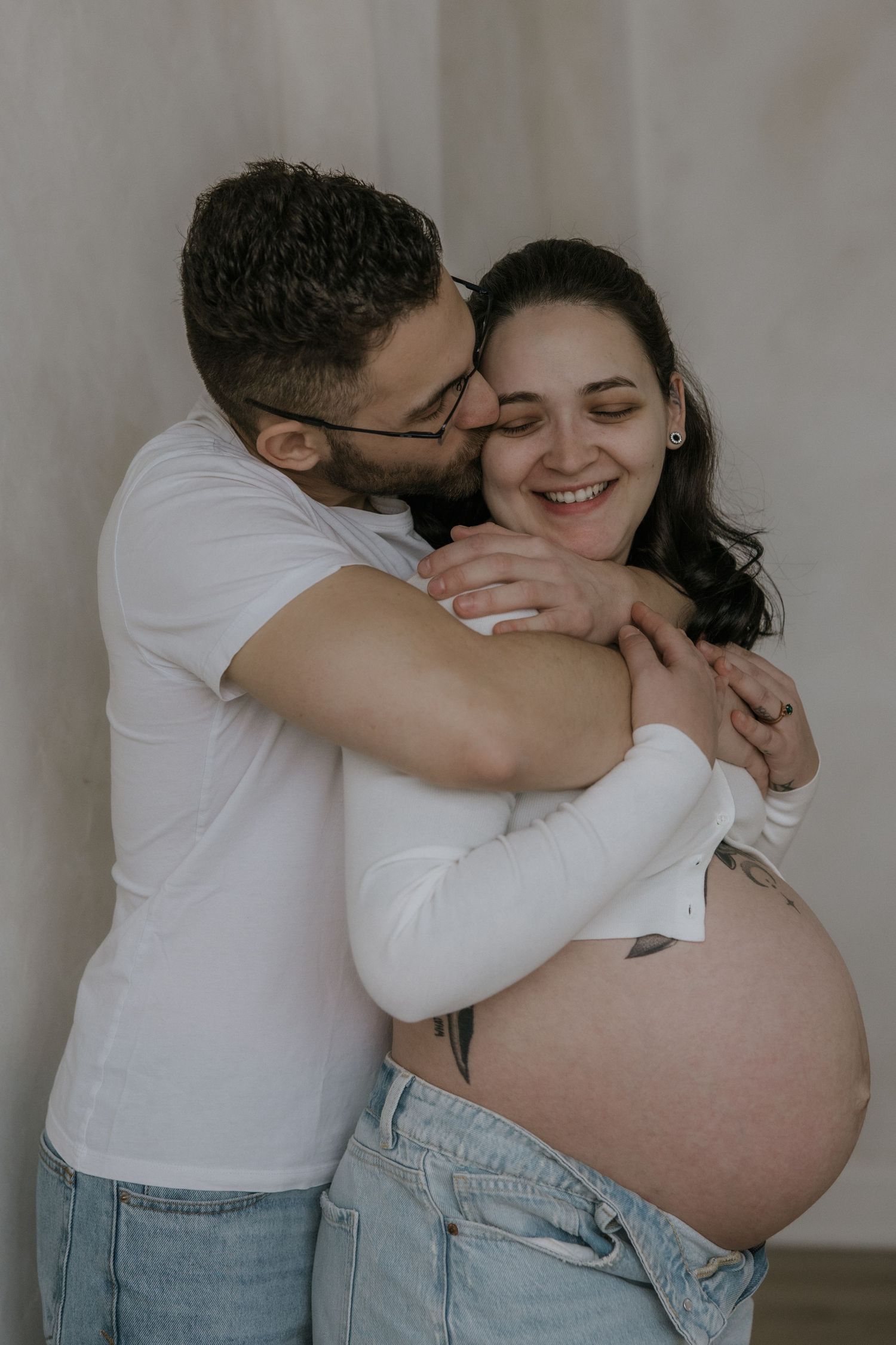 A tender pregnancy photoshoot sequence shows an intimate moment between a couple in white and denim against a neutral wall.