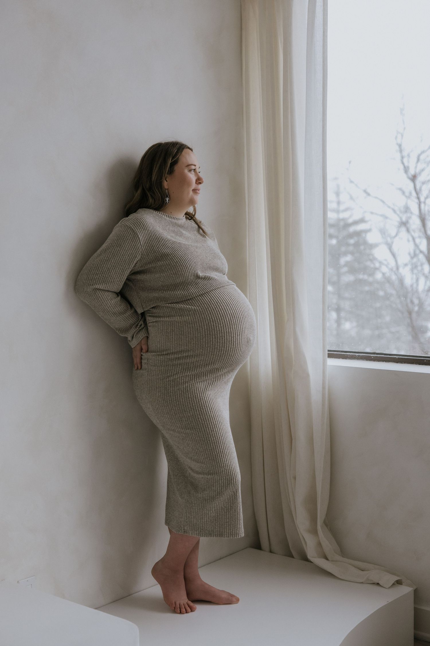 A series of artistic photos showing a person wrapped in a gray blanket standing by a window in moody lighting.